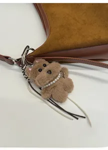 Detail of a brown plush dog charm with pearl necklace on a suede patchwork handbag