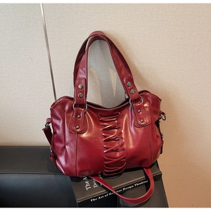 Detail of dark red punk tote bag with rivet accents and decorative cross straps on a sofa