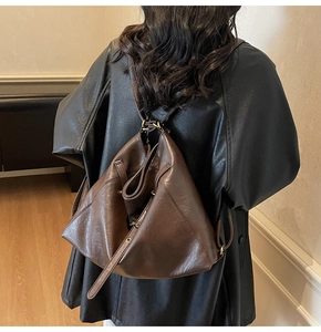 Detail of dark brown leather backpack with triangular fold design and bronze hardware