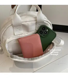 Detailed view of the front zipper pocket holding a green phone and pink wallet on white bag