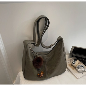 Detail of olive green hobo bag featuring contrast stitching and faux fur pompom charm