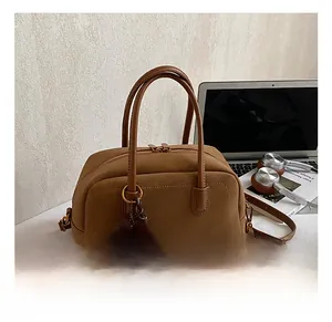 Detailed close-up of brown suede pillow bag featuring a fuzzy pom-pom and sleek brand logo