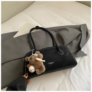 Detail of black matte shoulder bag with white contrast stitching and plush bear charm
