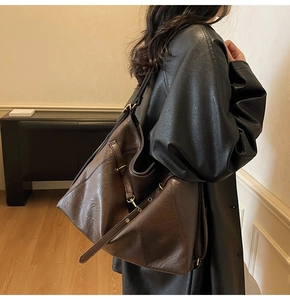 Detail of dark brown tote bag showing leather strap and metal buckle worn by model