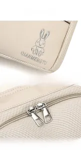 Detail of silver rabbit logo and dual metal zippers on beige backpack fabric