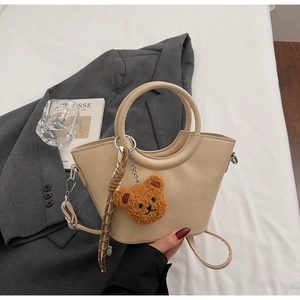 Dettaglio borsa a secchiello in pelle beige con manico tondo e ciondolo orsetto