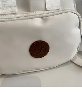 Detail of white canvas bag featuring a brown leather logo patch and precise stitching