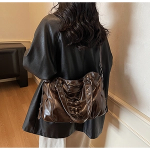 Detail of vintage brown tote bag featuring decorative rope lacing and metallic rivets