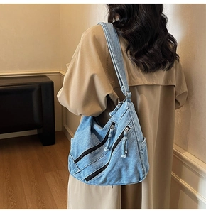 Detail of light blue denim hobo bag featuring decorative zippers and wide shoulder strap