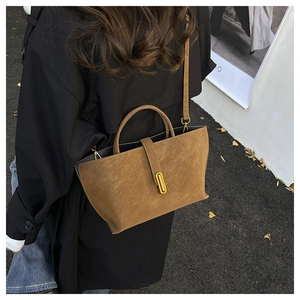 Detail of brown suede tote bag featuring a golden oval metal lock and adjustable strap