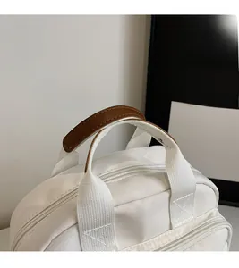 Close-up of durable woven handles with brown leather padding on a white square crossbody bag