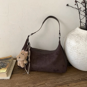 Detail of dark brown suede hobo bag with plush dog charm on a wooden table