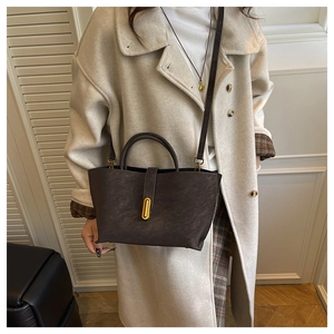 Detail of dark brown retro leather handbag with gold oval twist lock and long strap