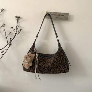 Close-up of leopard print dumpling bag with plush bear charm and black leather strap