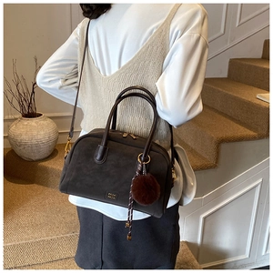 Detail view of dark brown suede pillow bag with plush charm and adjustable strap