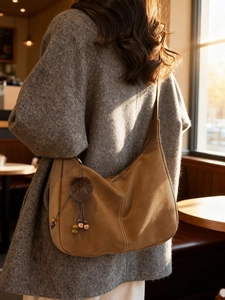 Brown suede dumpling tote bag with contrast stitching and plush charm on shoulder