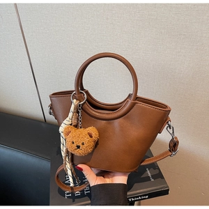 Dettaglio borsa a secchiello in pelle marrone con ciondolo orsetto e foulard a righe