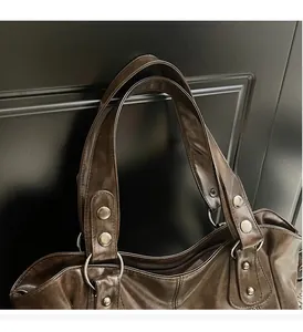 Détail du sac cabas en cuir souple montrant les rivets métalliques et la large bandoulière