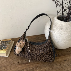 Detail view of leopard print shoulder bag with a cute plush bear charm on a vintage desk