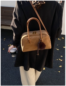Brown suede Boston bag with double handles and fur pom-pom charm on an autumn street