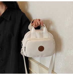 Close-up of white canvas crossbody bag with brown leather logo patch and zipper