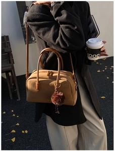 Close-up of brown Boston bag with plush ball charm and gold zippers in street style shot