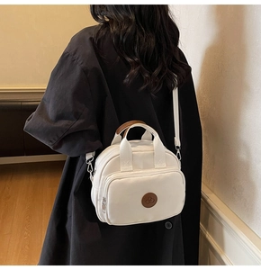 Rear view of a model carrying a white nylon crossbody bag with brown leather handles