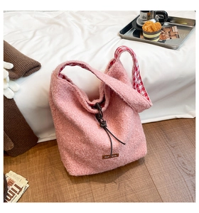 Pink fleece tote bag with red plaid lining and leather label in cozy home setting