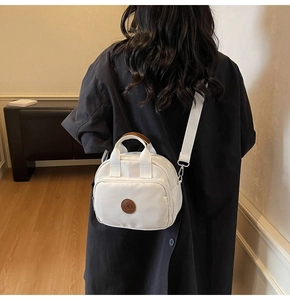 Detail of white nylon crossbody bag with brown leather logo patch on female model