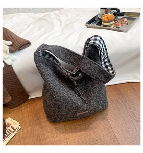 Detail of grey plush tote bag featuring checkered lining and drawstring on a cozy bed