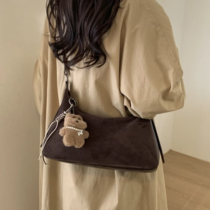 Detail of dark brown suede baguette bag with a plush bear charm on a trench coat