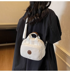 White canvas crossbody bag with brown leather logo patch and handle detail on a model