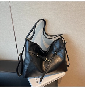 Detail view of large black leather hobo bag with gold buckles on artistic book background