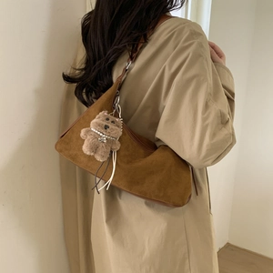 Detail of brown suede dumpling bag featuring a cute plush bear charm on the shoulder strap