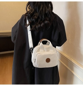 Detail of white canvas crossbody bag with brown leather handles worn by model in casual style