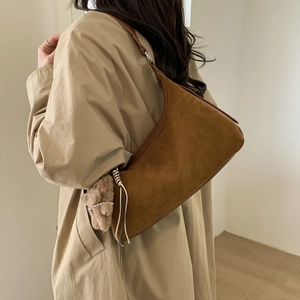 Close-up of brown suede moon bag featuring a cute teddy bear charm on model's shoulder