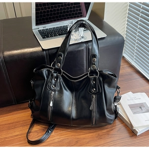 Détail d'un sac cabas en simili cuir noir avec zips argentés sur fond en bois