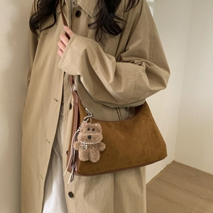 Brown suede hobo bag shown on shoulder with teddy bear charm and camel coat