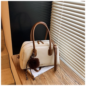 Detail of cream and brown boston bag with plush charm and soft shadow lighting