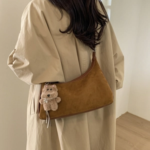 Close-up of brown suede dumpling bag with leather trim and plush bear charm on a shoulder