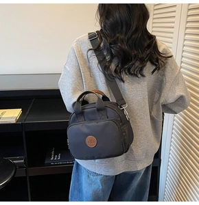 Side view of black nylon crossbody bag with cherry logo and brown leather handles