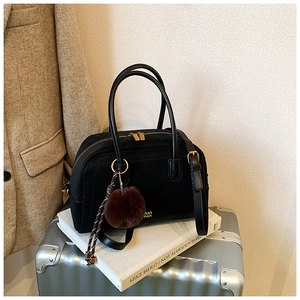 Detail of black pillow bag with gold hardware and plush charm on a silver suitcase
