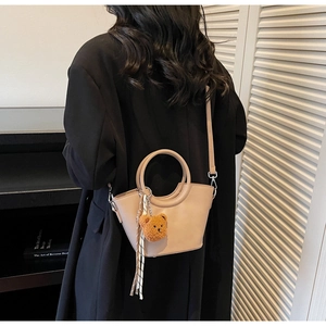 Dettaglio della borsa a secchiello beige con ciondolo a orsetto sulla schiena della modella