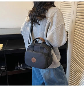 Detail of a black nylon crossbody bag with leather handles and a round logo patch