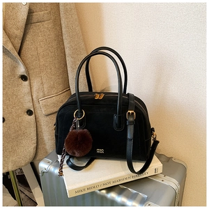 Close-up of black Boston bag with gold hardware and plush charm on travel luggage