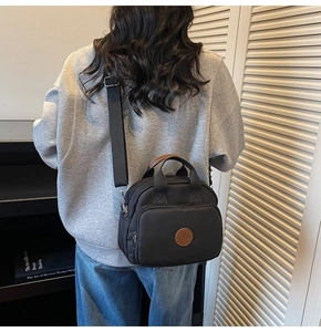 Detail of black crossbody bag with brown leather logo patch on a casual nylon finish