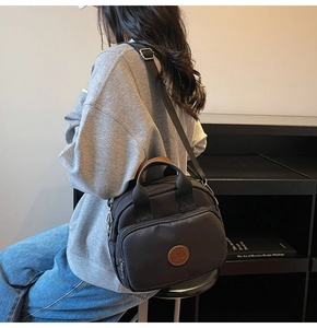 Detail of black canvas crossbody bag showing front zipper and brown leather patch