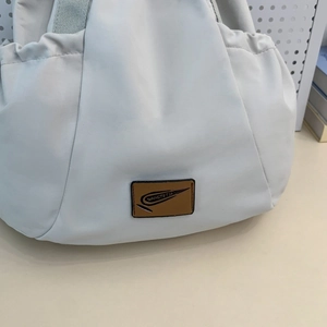 Close-up of the light gray fabric bag featuring a brown leather brand logo patch