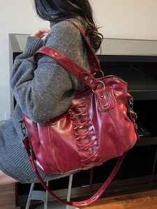 Large burgundy tote bag with lace-up punk design shown on shoulder in a cozy interior