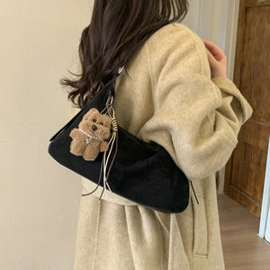 Detail of black suede croissant bag with teddy bear charm and beige tassel detail